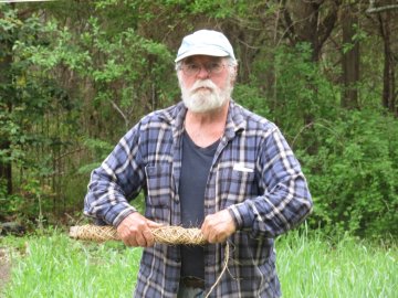 Man wrapping twine on a stick, gazing at camera with a serious look